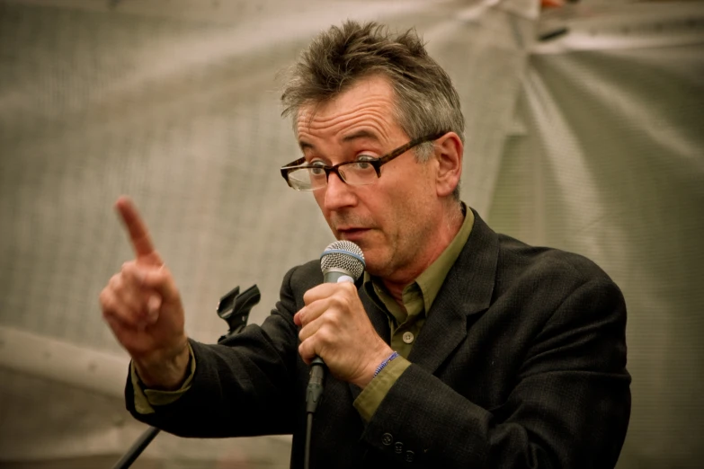 a man in glasses holds a microphone up while talking