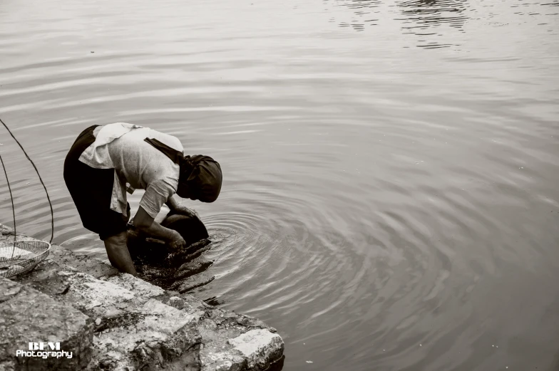 an old man with a hat bending over to cool down by a pond