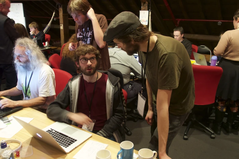 a man looking at a laptop surrounded by people