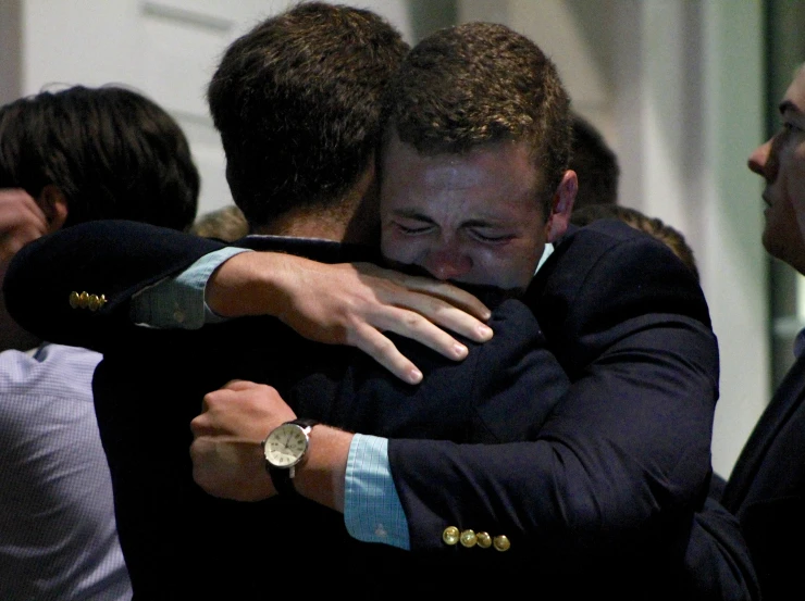 two men in suits hugging each other outside