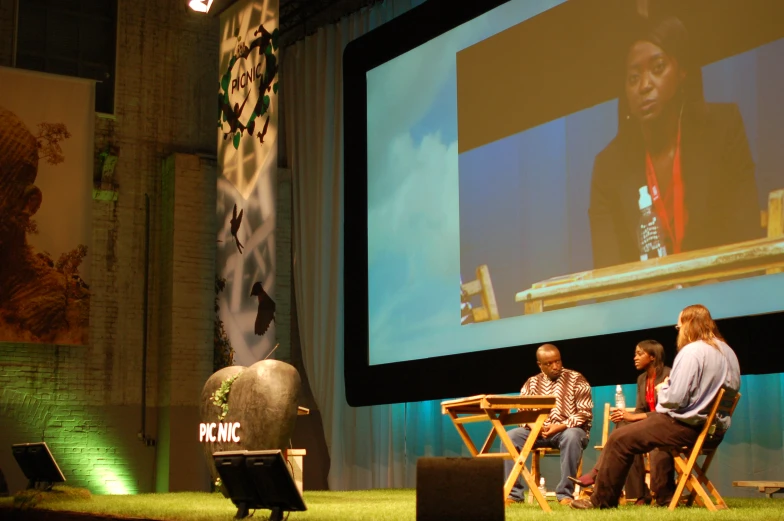 four people sitting in folding chairs and two watching a large screen