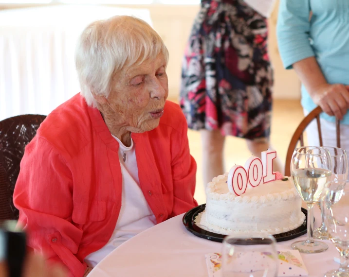 an elderly woman blowing out candles on her birthday cake