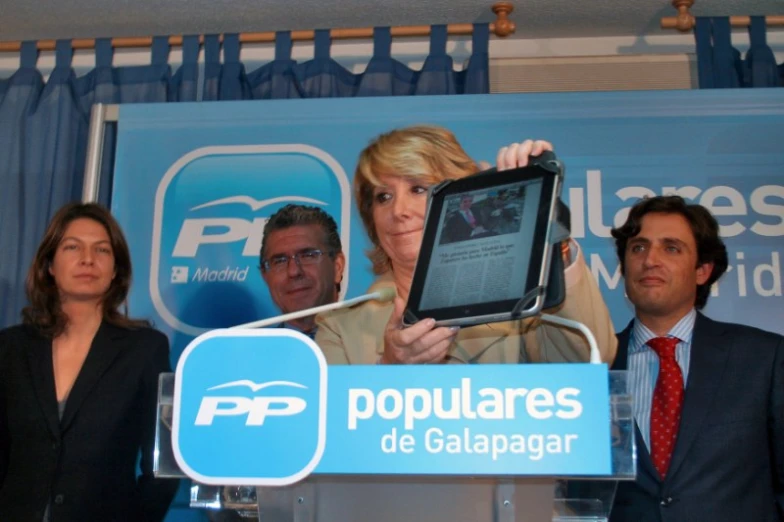 a woman holds up a tablet as two men stand beside her