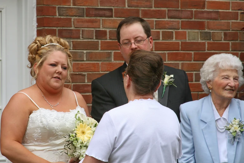 a woman in a wedding dress holding flowers and talking to an older man