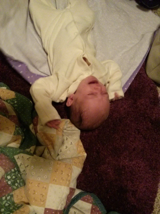 baby wrapped in blanket laying on purple fabric