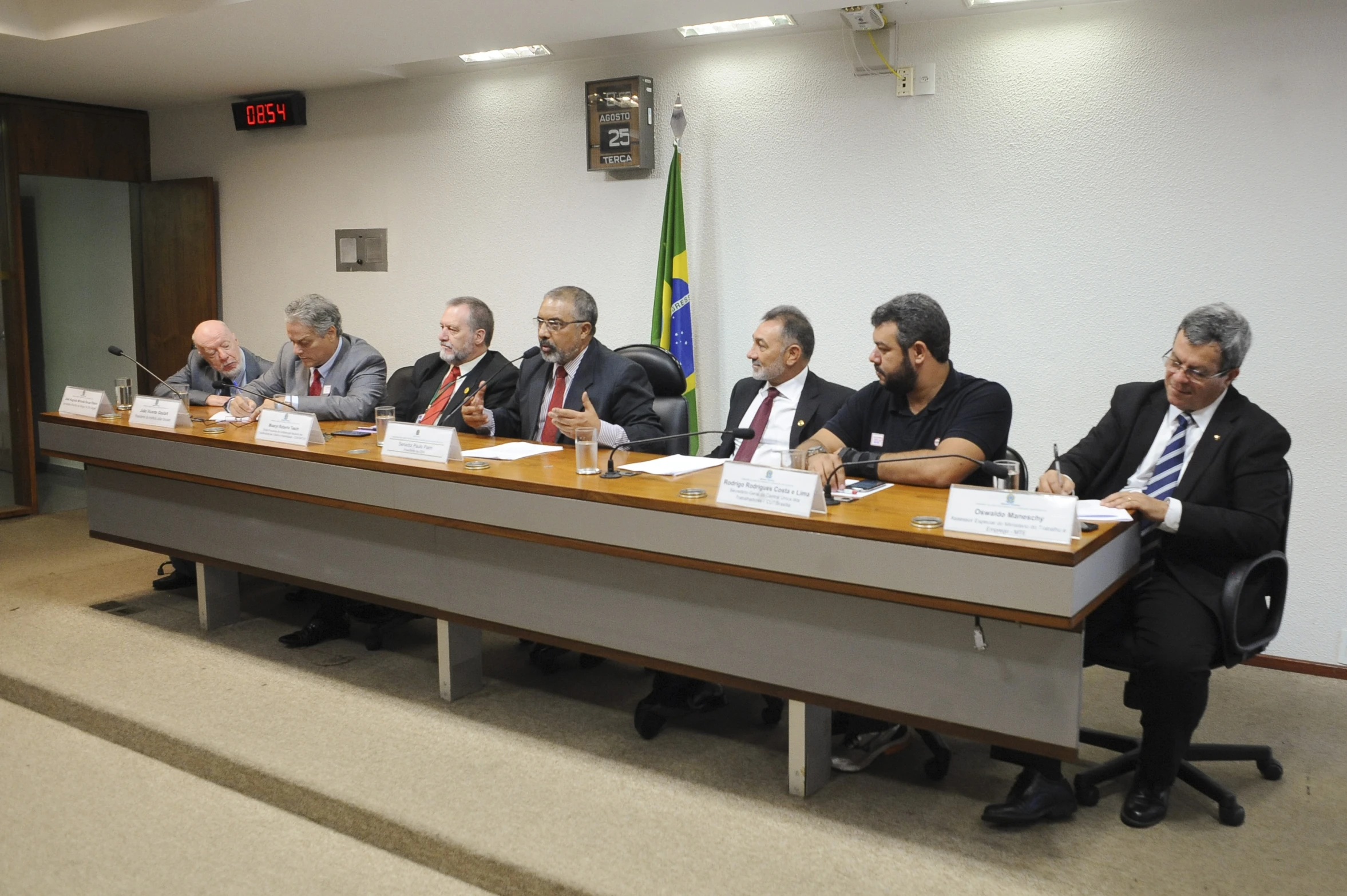 five men sit at a desk with papers