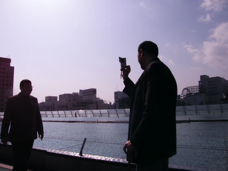 two men standing by the water with one holding a cell phone