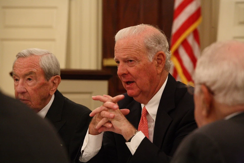 an older gentleman in a suit speaks to others