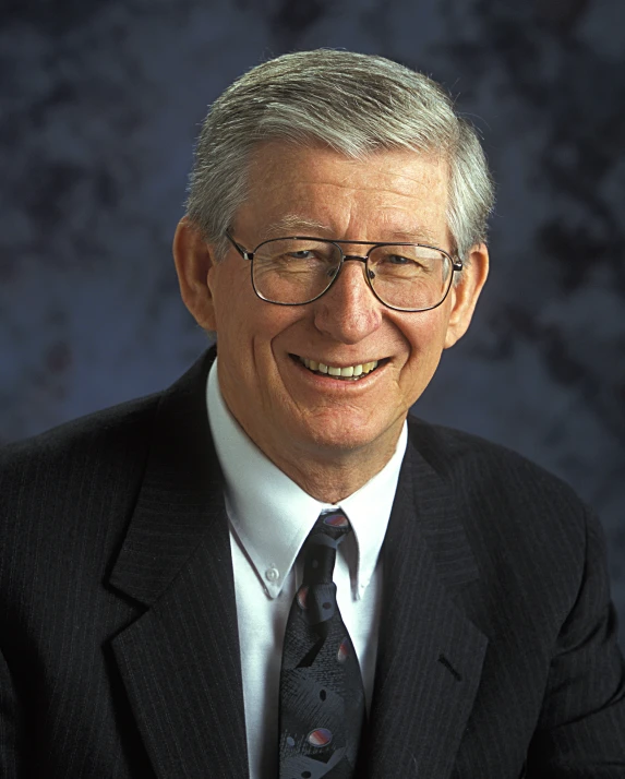 an old man wearing glasses and a tie smiles