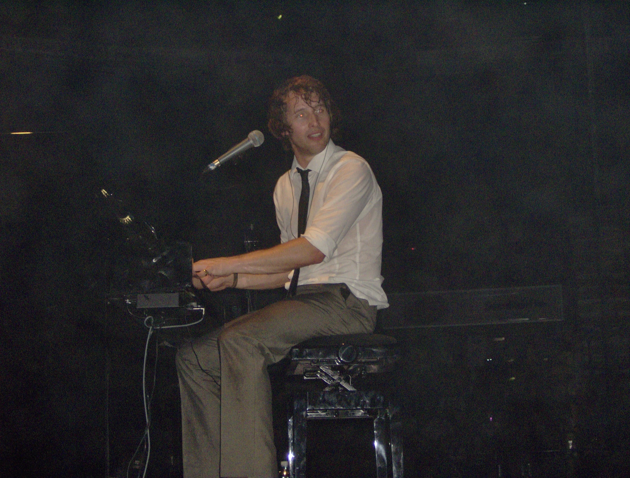 a man in tie and black shoes on a stool holding a microphone