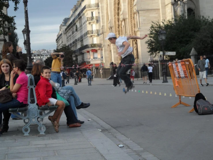 a man jumps in the air over two benches as pedestrians look on