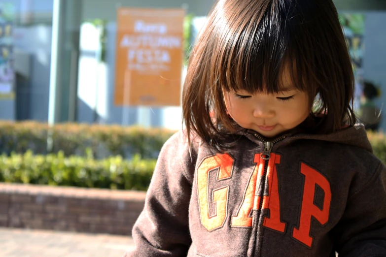 a little girl is wearing a hoodie and looking down