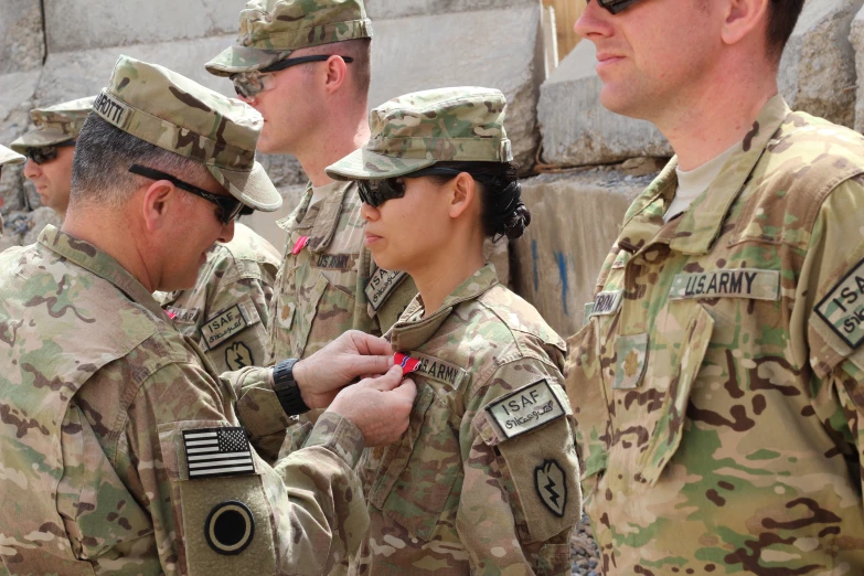 women in military fatigues put their medals on by men in the background