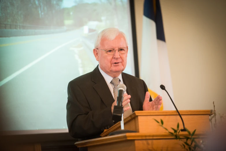 an old man is giving a presentation at a podium