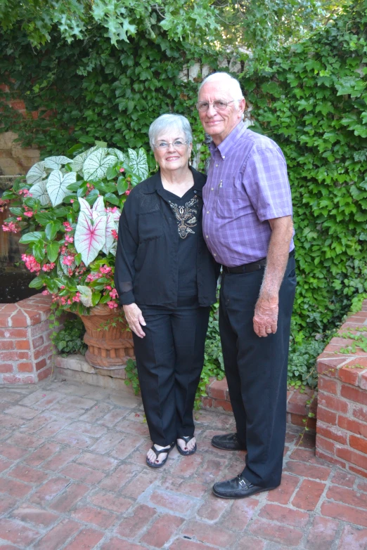 a woman and an elderly man standing in front of bushes