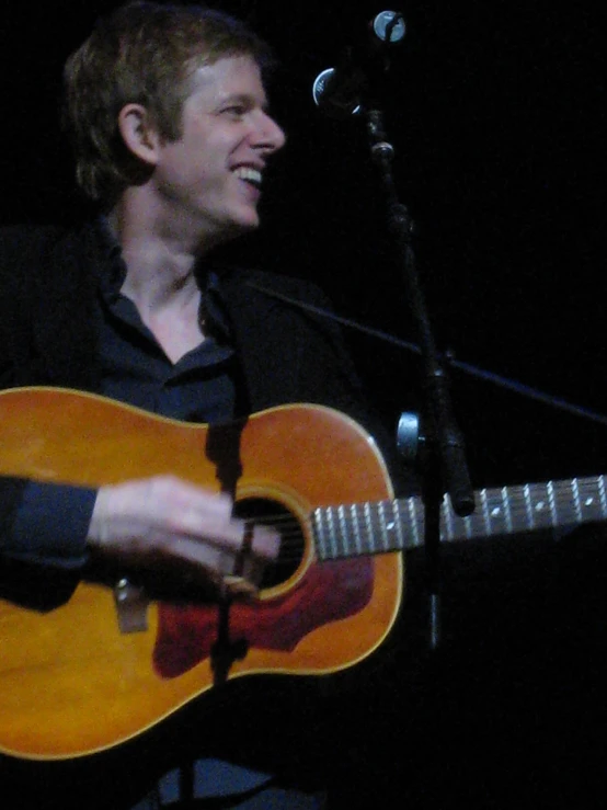 a man holding a guitar stands in front of a microphone