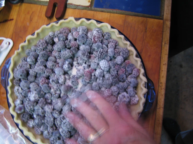 a hand touching a pie crust in a pie pan