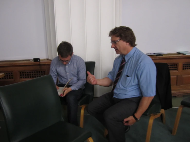 two men sitting in chairs holding pens and papers