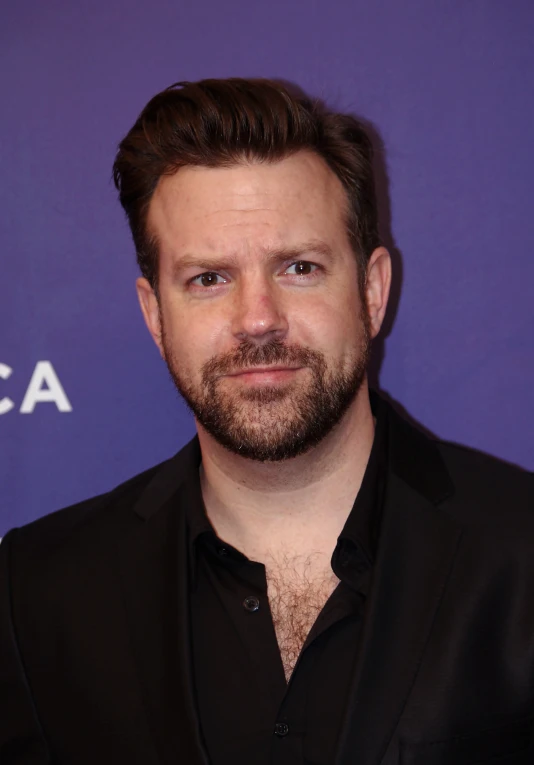 a man with a goatee in a black suit and dark shirt