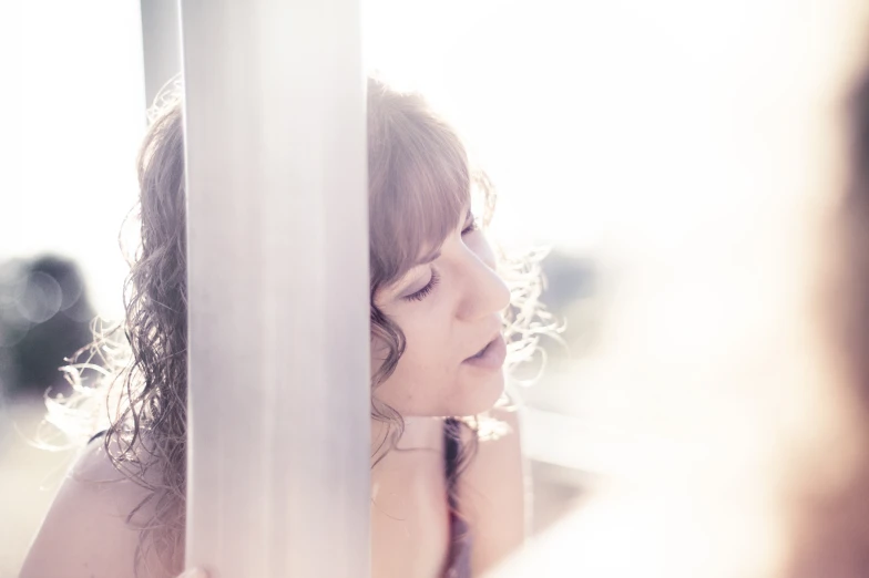 a woman leans against a pole while staring away from the camera