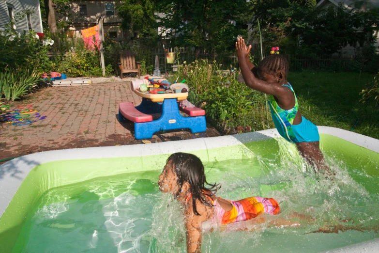 two s in the backyard splashing in a green pool