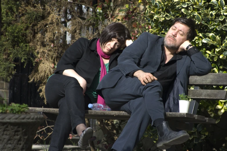 two people sitting on a park bench looking bored