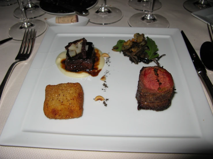 a square plate of food is sitting on a table with wine glasses