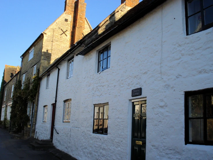 a building with three windows is shown in the foreground and some brick buildings, along with the sun shining through