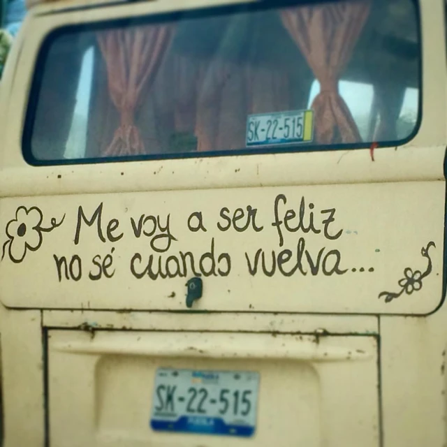 the back side of an old yellow vehicle with a graffiti message written on the window