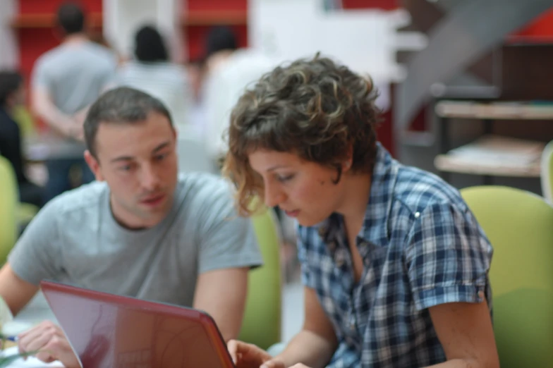 two people sit in front of a laptop computer while one uses it