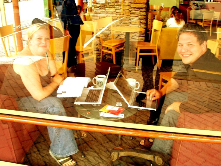 two people smiling at a table with a laptop