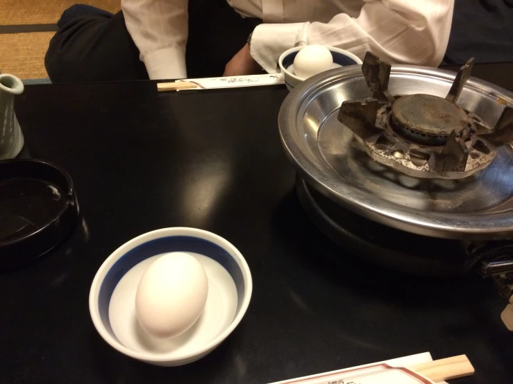 some people are sitting around at a table with bowls and an egg on top