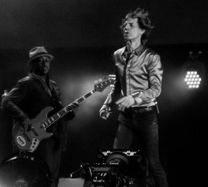 a person standing on stage playing a guitar and another guy in the background