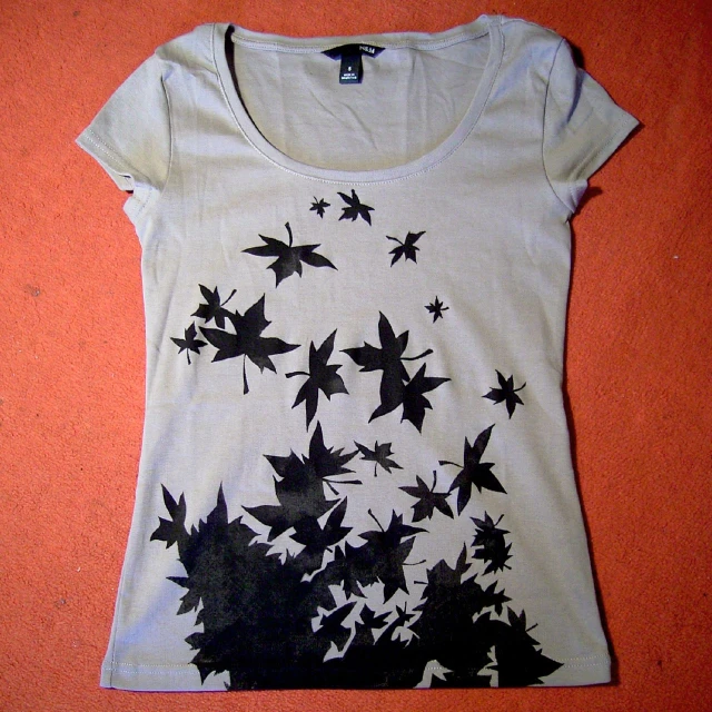 a womans white tee shirt with black leaves flying out of it