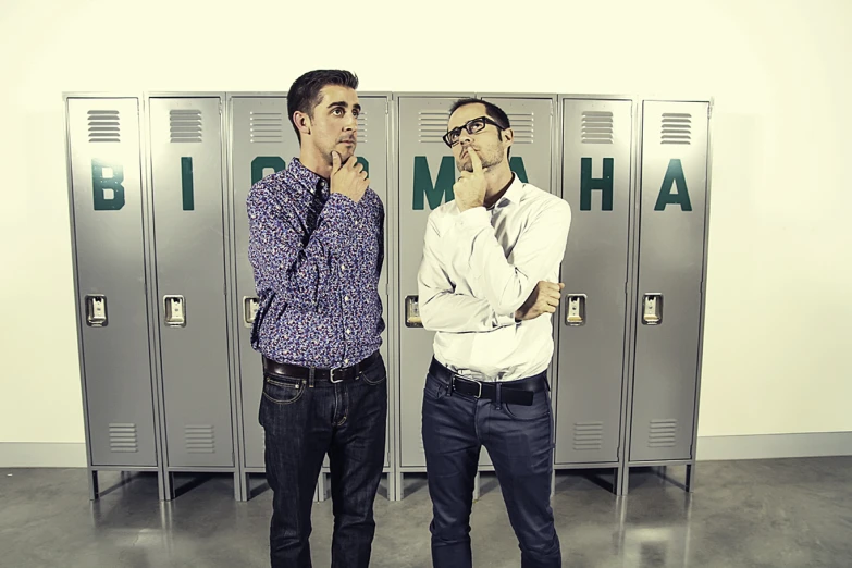 two men standing in front of metal lockers with their hands under their mouths
