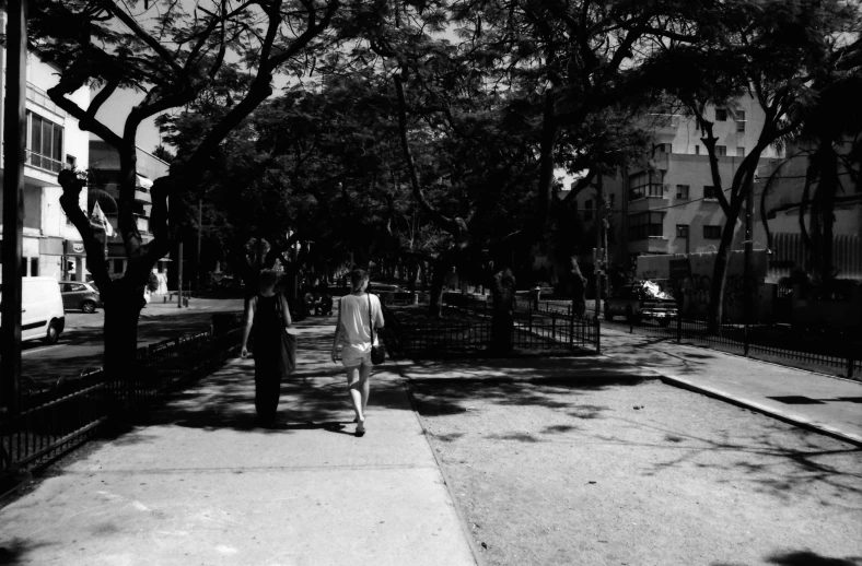 two people walking down a sidewalk between tall buildings