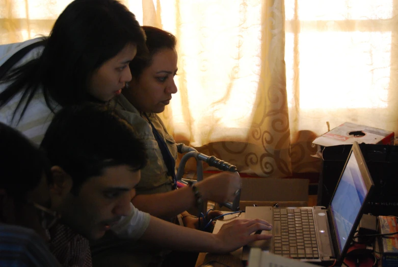 three people sit next to each other at a desk working on laptops