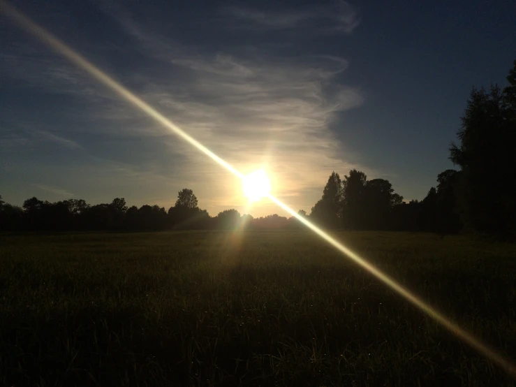 the sun is setting behind the trees on a grassy field