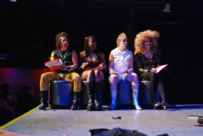 three young women sitting on stools in an audience