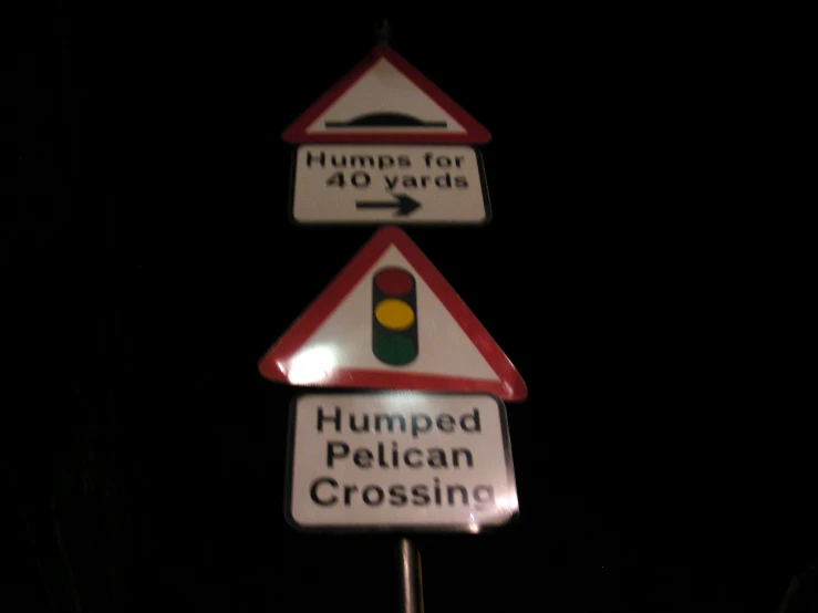 three street signs in the dark that say humped pelican crossing and humps for 40 yards