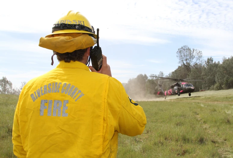 a fireman with a hose attached to his waist, wearing yellow and carrying a small radio camera in front of an air plane