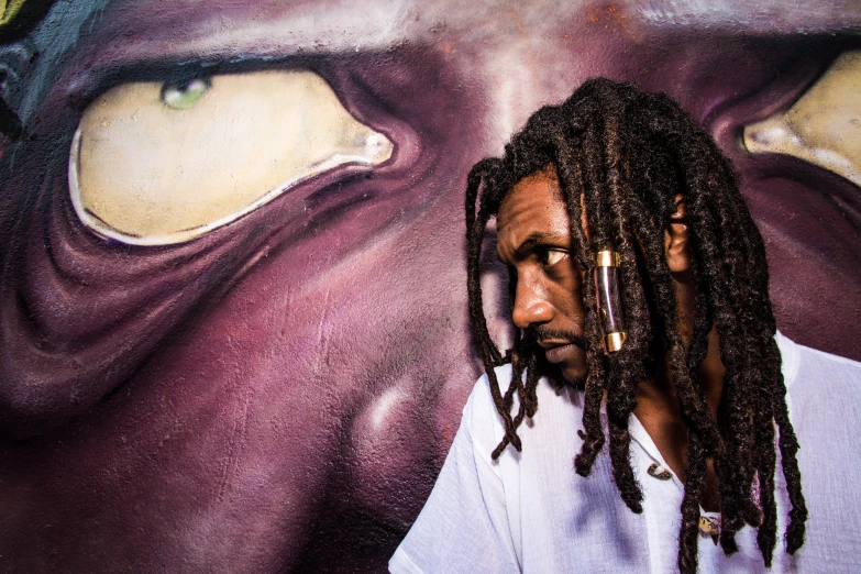 a man with dreadlocks standing next to some colorful walls