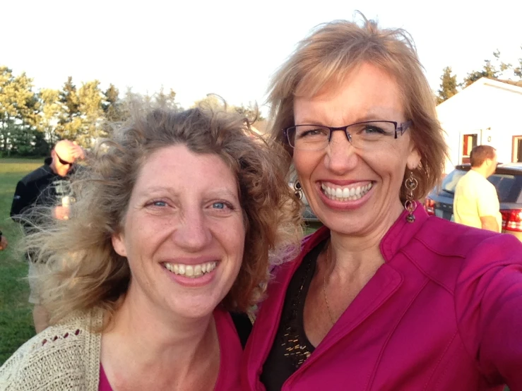 two women are smiling in front of an outdoor gathering