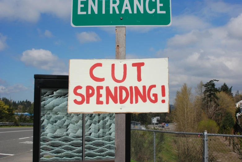 a sign saying cut spending with a background of a fence