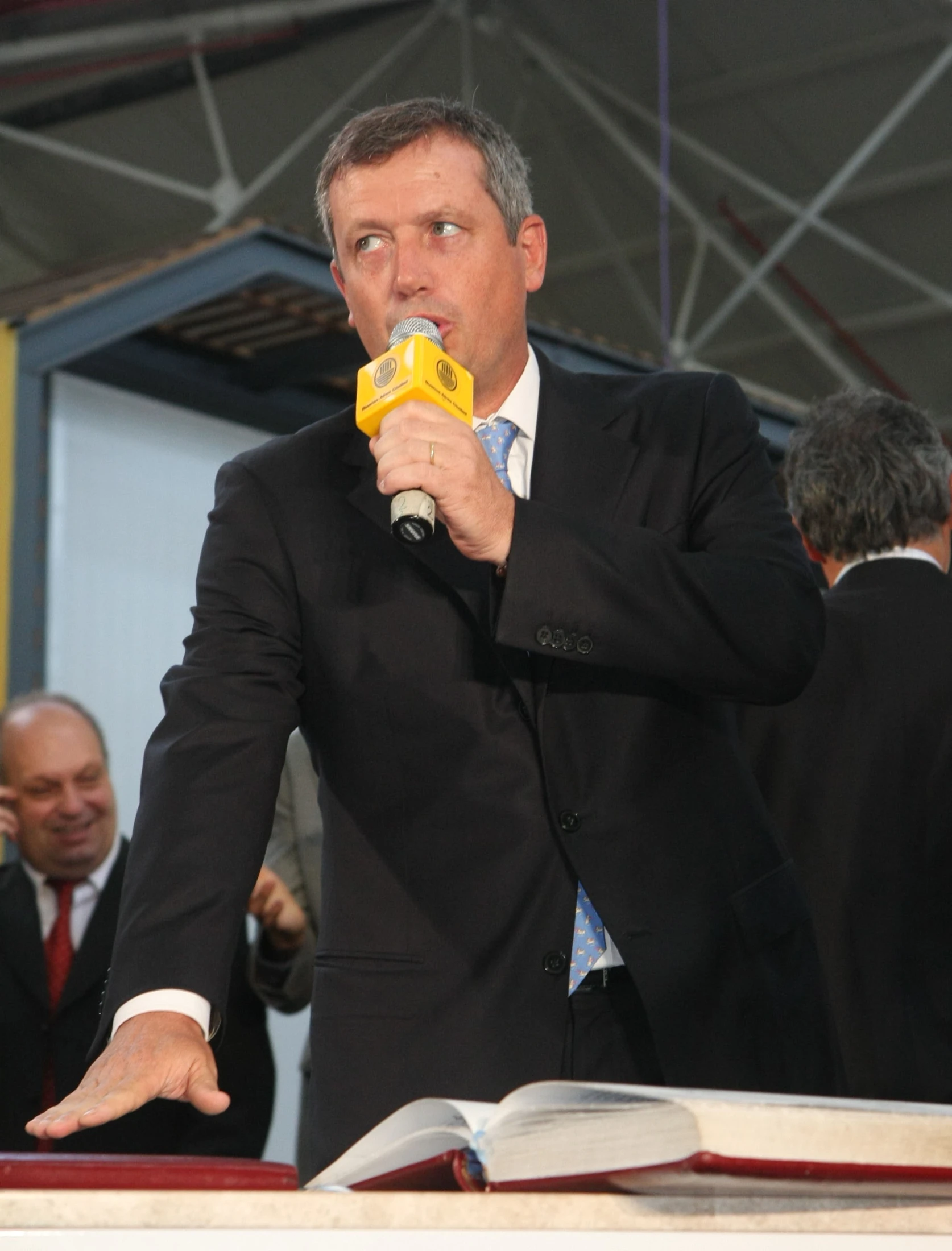 a man speaking on a microphone next to an open book