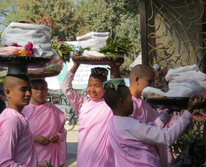 many children in buddhist clothing are carrying food on their heads