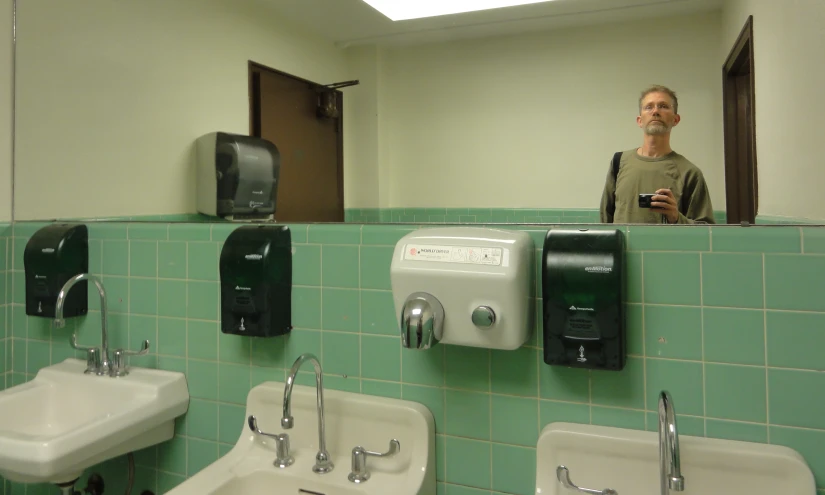 a guy is taking a po in the mirror and he is looking at some stalls in the restroom