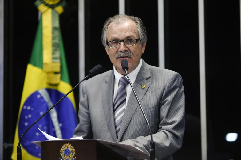 man at podium with flag in background during speech