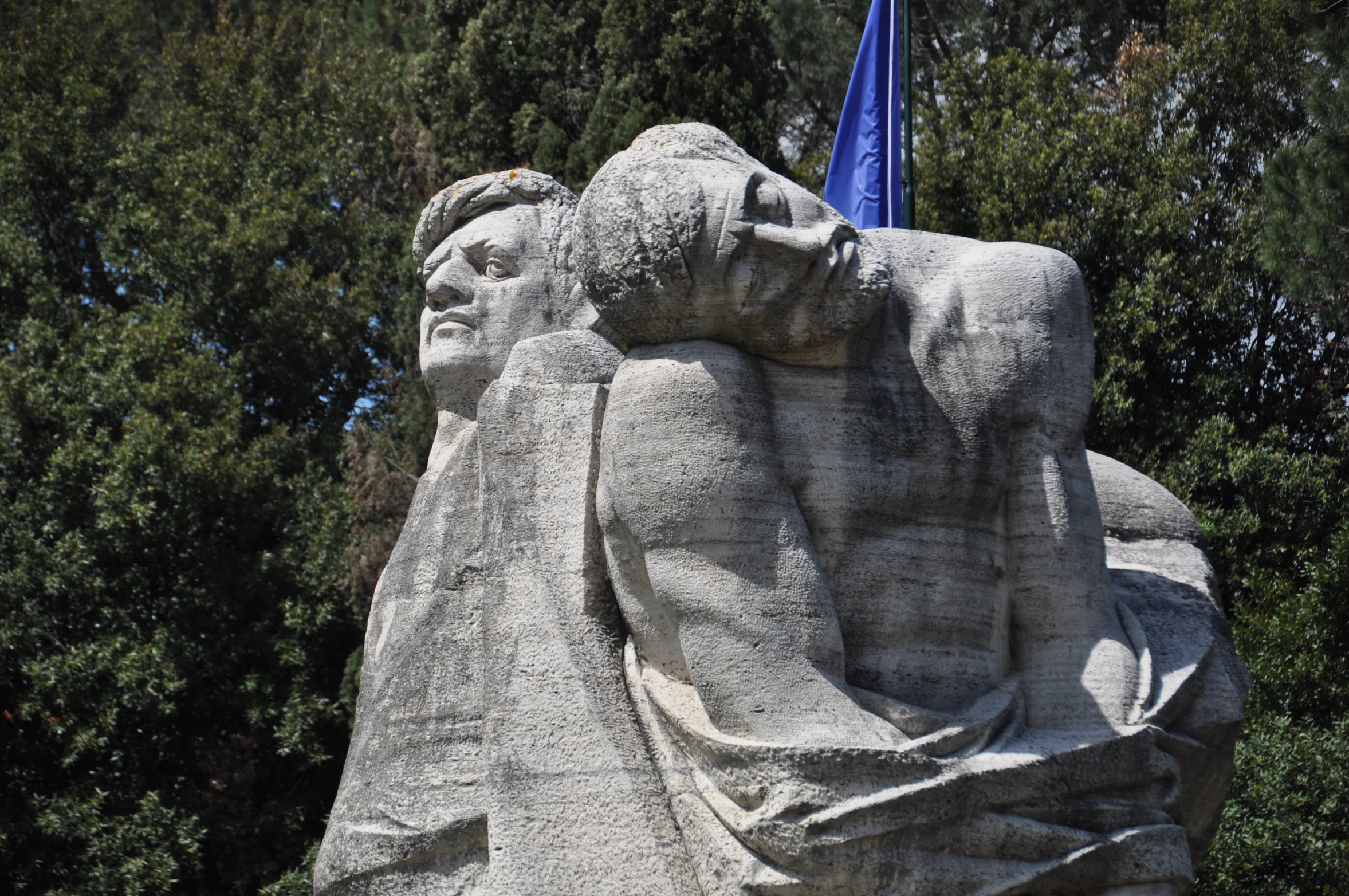 a statue of two men and a flag on a tree filled hill