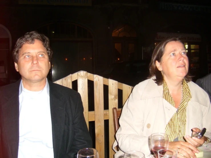 a woman sitting next to an old man in front of a wooden fence